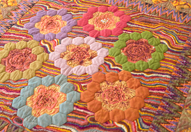 Kaffe Fassett and Liza Lucy  work together to create a masterful medallion quilt in rich, warm tones. The quilt begins with a stunning medallion center that is comprised of English paper-pieced hexagon rings and hand-appliqued fussy-cut fabrics. 